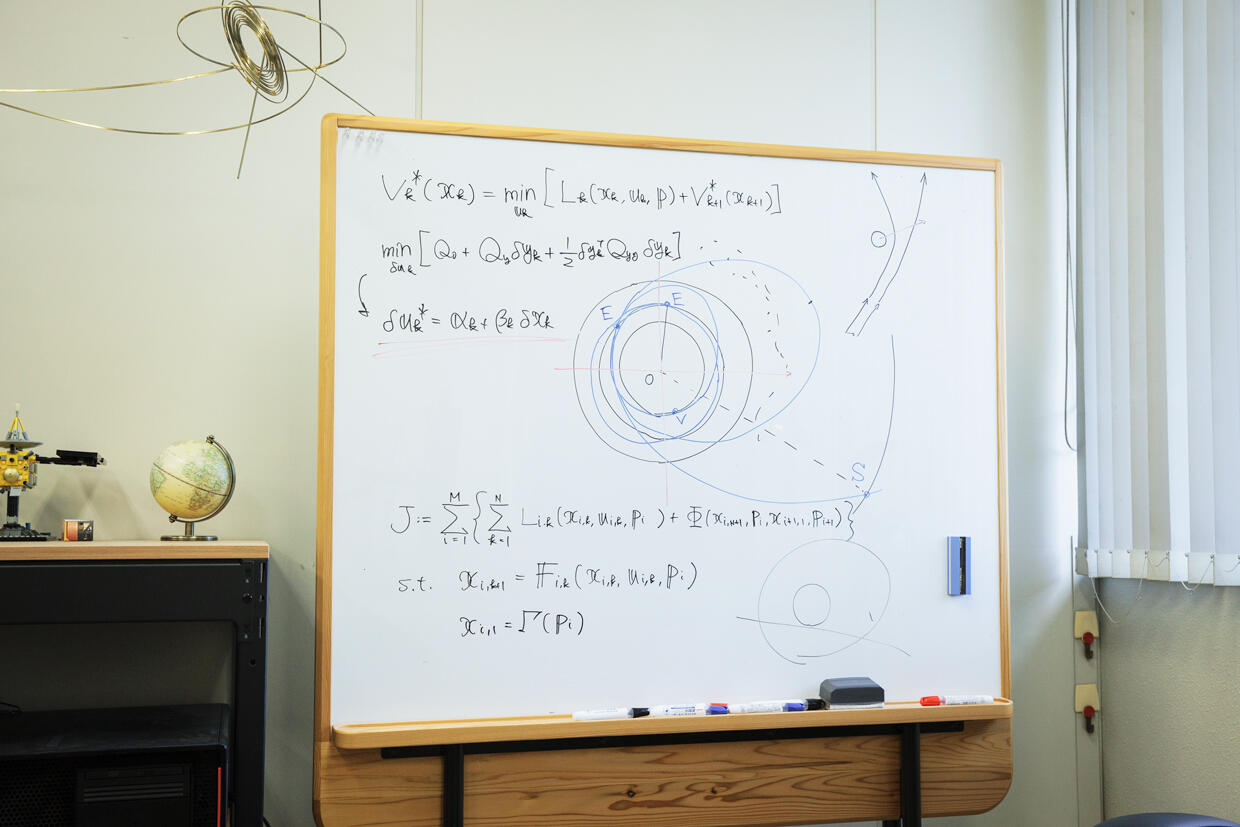 On the whiteboard in Ozaki's laboratory are mathematical formulas for trajectory design