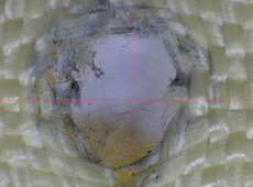 Hole made when a projectile was fired at spacesuit fabric.