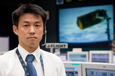 Flight Director Takayoshi Nishikawa in the Kibo Mission Control Room. On the monitor screen behind him is the HTV docked with the ISS.
