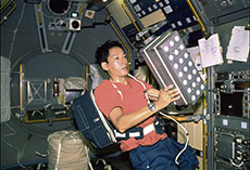 Astronaut Mamoru Mouri holding a rack of chicken eggs and conducting an experiment (courtesy: JAXA/NASA)